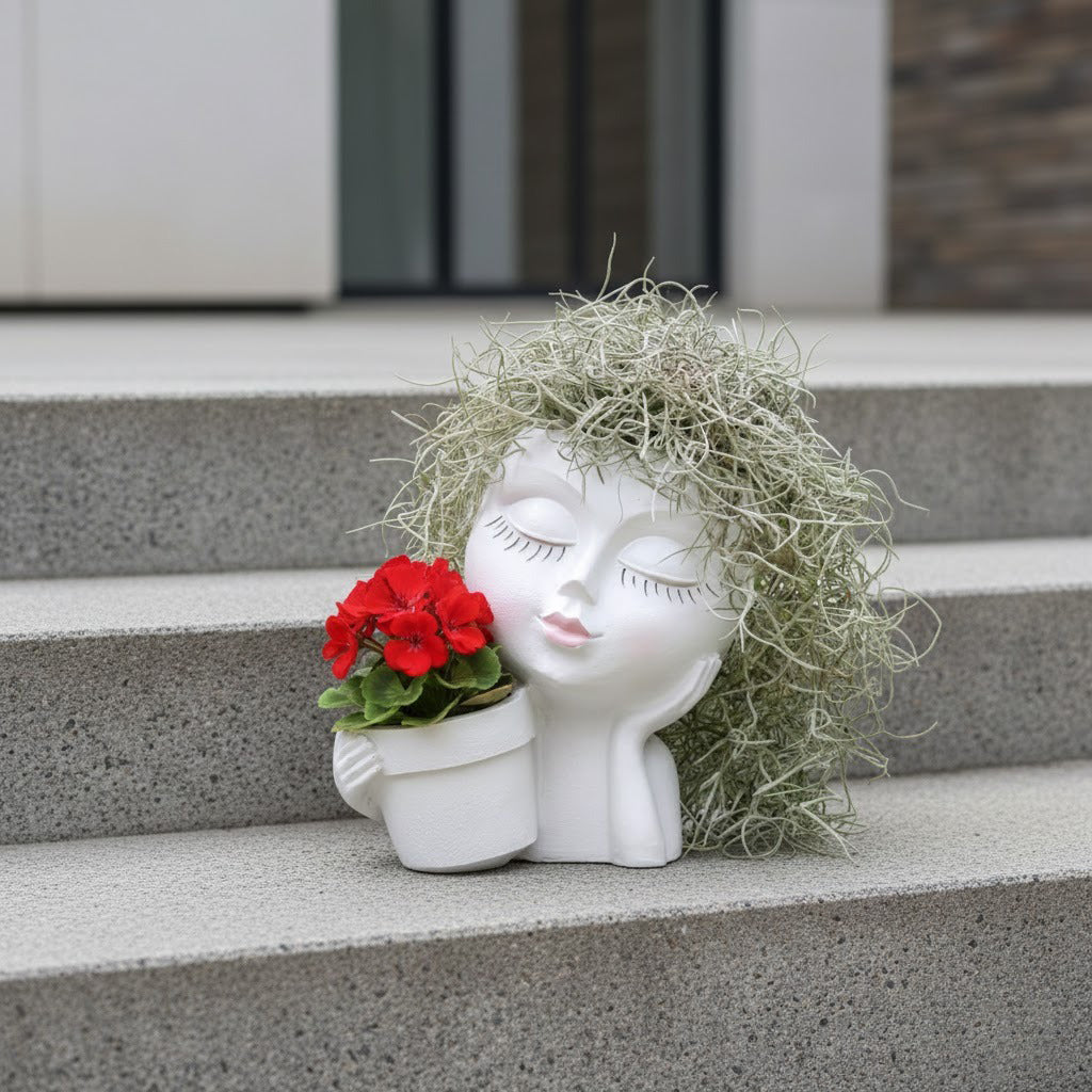 White head-shaped planter with red flowers and greenery on concrete steps