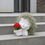 White head-shaped planter with red flowers and greenery on concrete steps