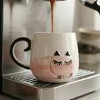 Cat-shaped mug being filled with coffee from an espresso machine.