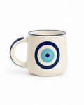 An off-white ceramic mug with a navy blue rim and handle, featuring a blue and light blue concentric circle evil eye design on the front.