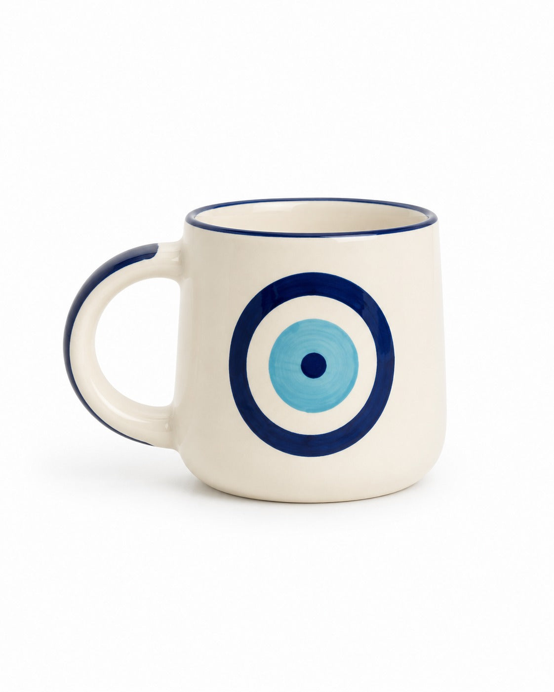 An off-white ceramic mug with a navy blue rim and handle, featuring a blue and light blue concentric circle evil eye design on the front.