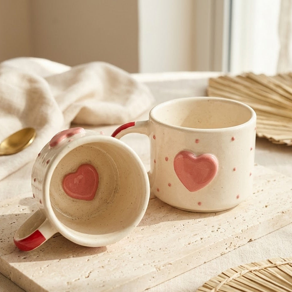 Two ceramic mugs with heart designs on a light surface.