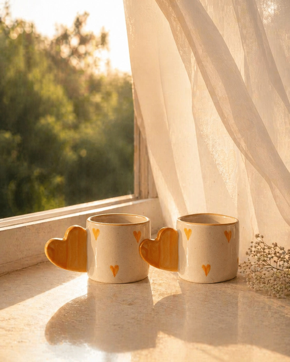 Three ceramic mugs with heart designs on a windowsill with a view of trees.