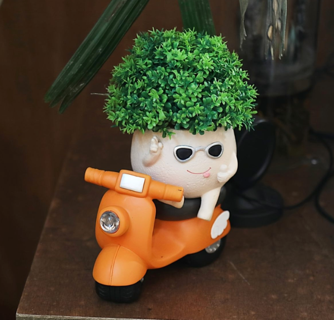 Decorative planter shaped like a cartoon character on a scooter with greenery on top