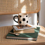 Ceramic mug with black polka dots on a stack of books on a woven surface