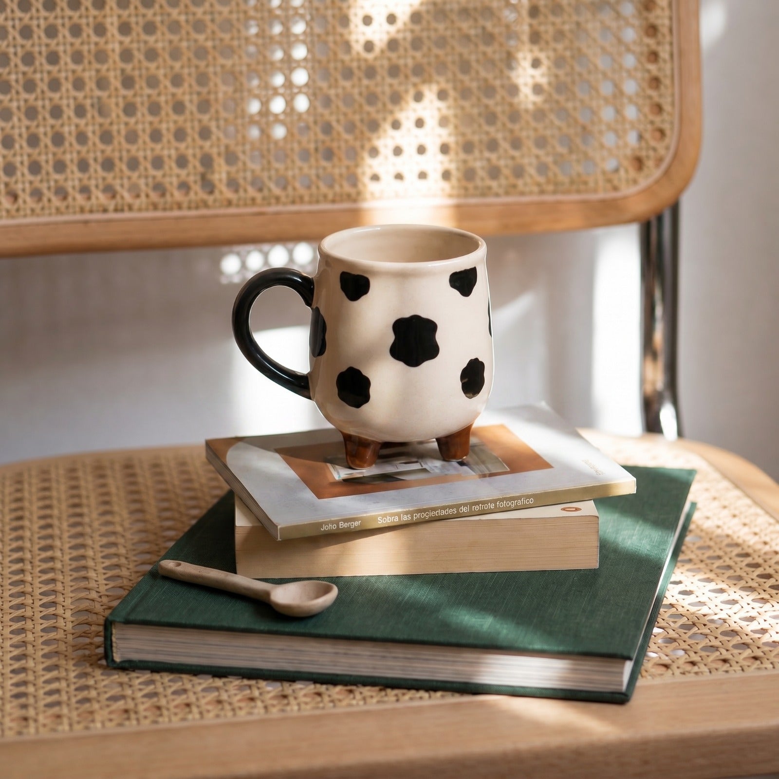 Ceramic mug with black polka dots on a stack of books on a woven surface