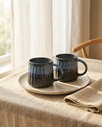Two dark blue ceramic mugs on a light wooden table with a neutral background