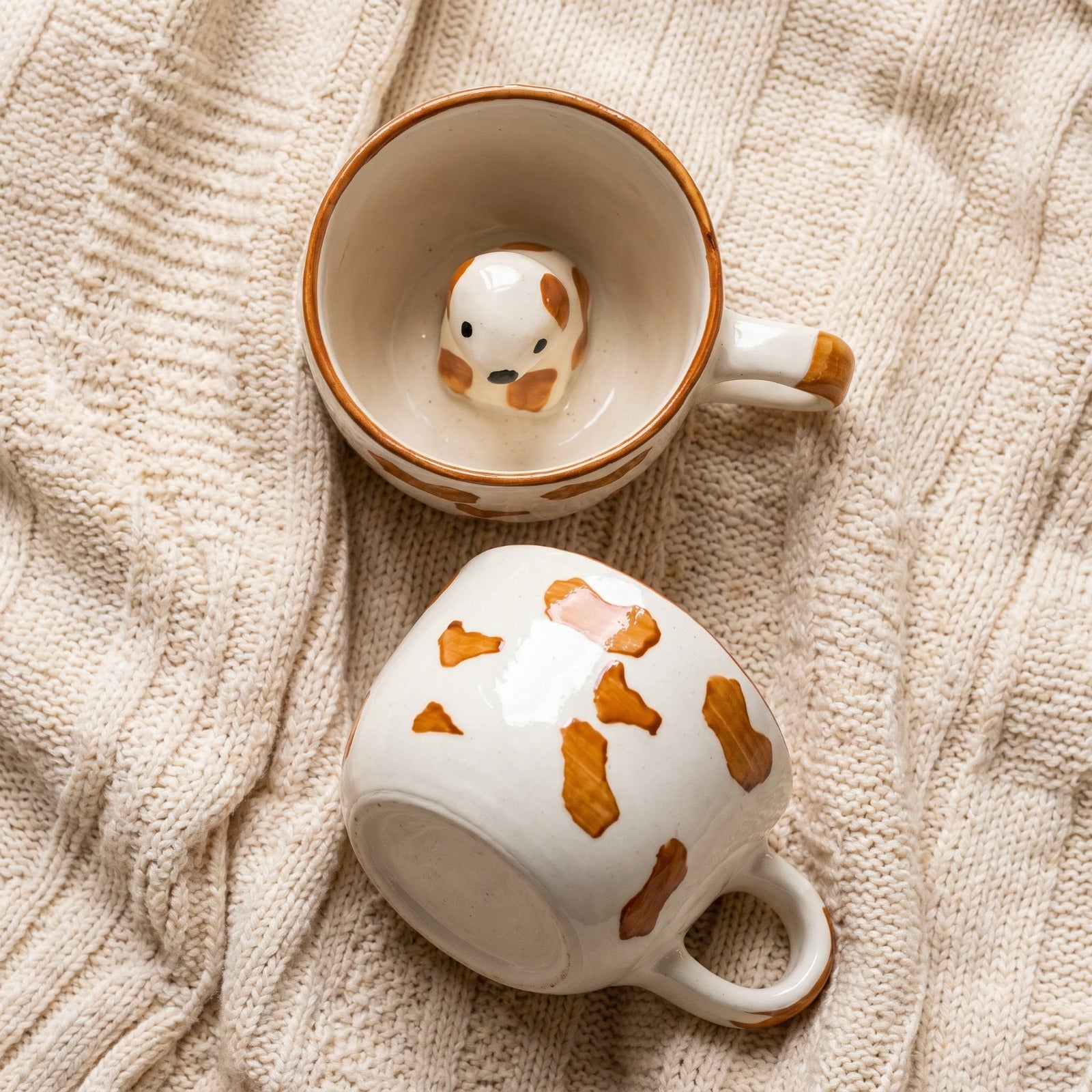 Two ceramic mugs with dog designs on a textured beige surface