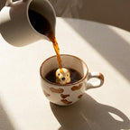 White ceramic cup with brown paw prints being filled with coffee, featuring a small dog-shaped object下沉.