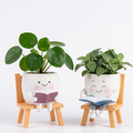 Two decorative planters with smiling faces sitting on small wooden chairs, reading books.