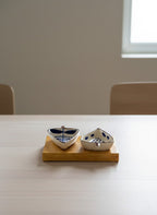 Two ceramic boats on a wooden stand on a white table with a blurred background