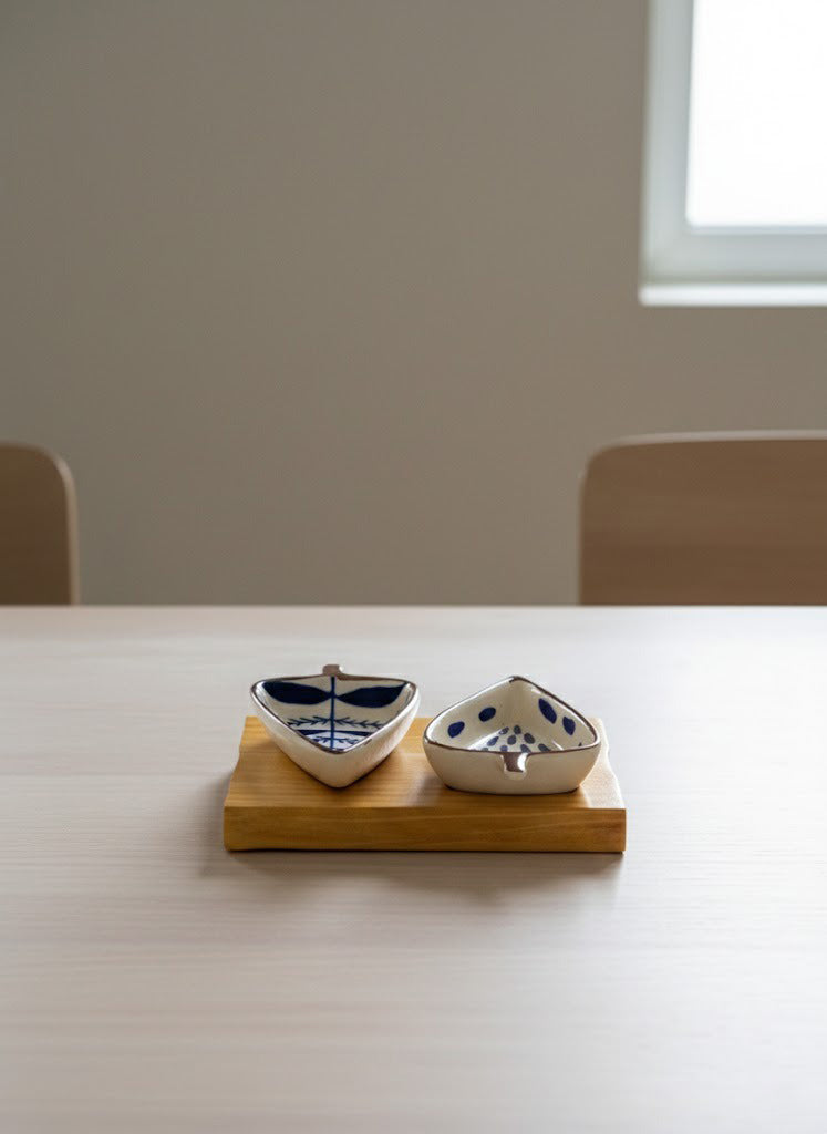 Two ceramic boats on a wooden stand on a white table with a blurred background