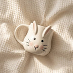 Ceramic mug shaped like a rabbit face on a textured beige surface