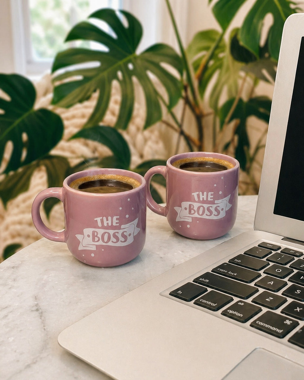 Two pink mugs labeled 'The Boss' on a laptop with a plant in the background