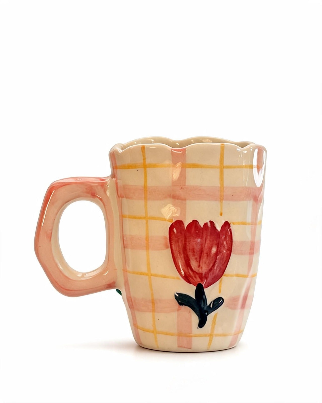 A small ceramic mug with a scalloped rim, a peach-colored handle, and a cream body decorated with a yellow plaid pattern and a red tulip with a black stem.