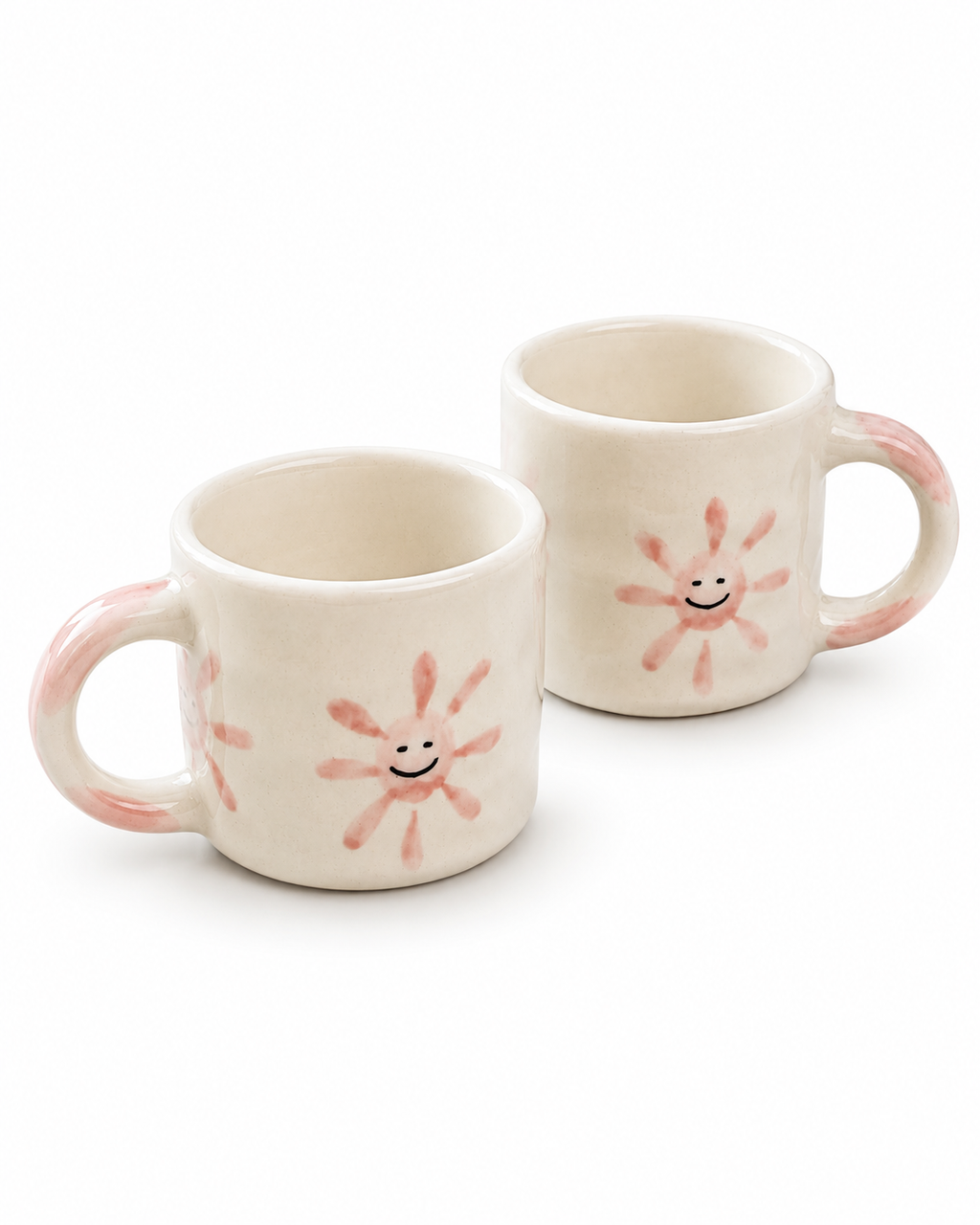 Two cream-colored ceramic mugs with pink hand-painted sunflower designs and smiling faces, set against a plain white background.