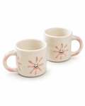 Two cream-colored ceramic mugs with pink hand-painted sunflower designs and smiling faces, set against a plain white background.